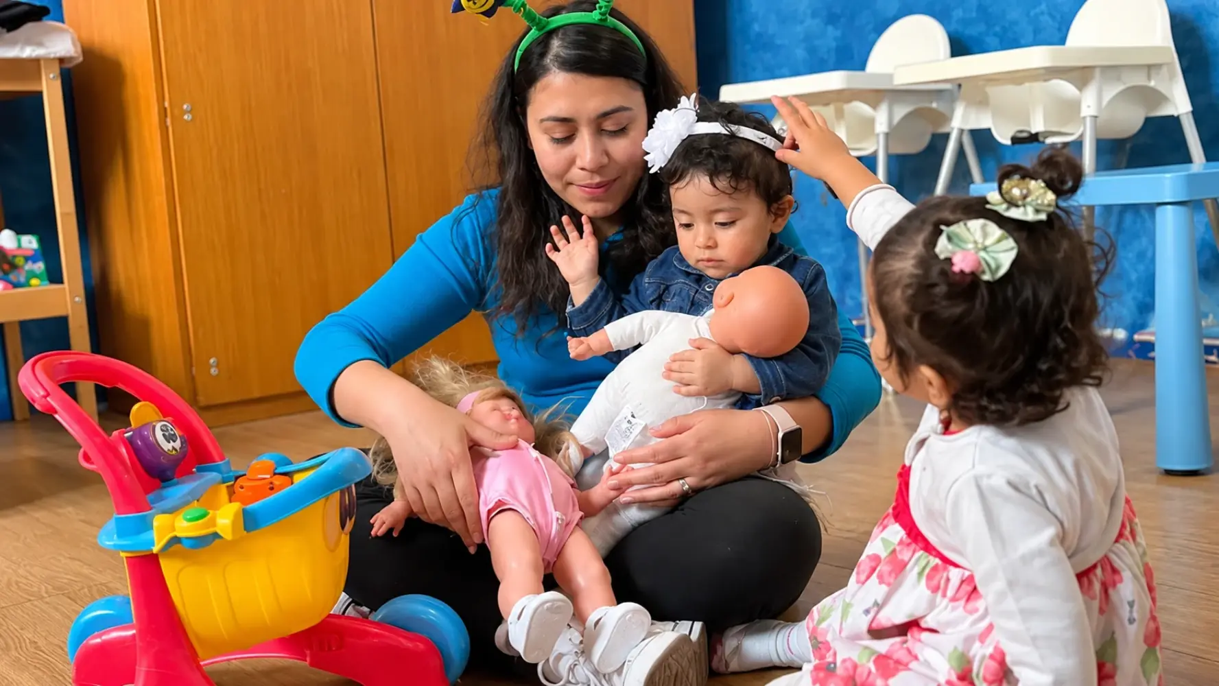 Una maestra con tres niños pequeños que juegan con muñecas