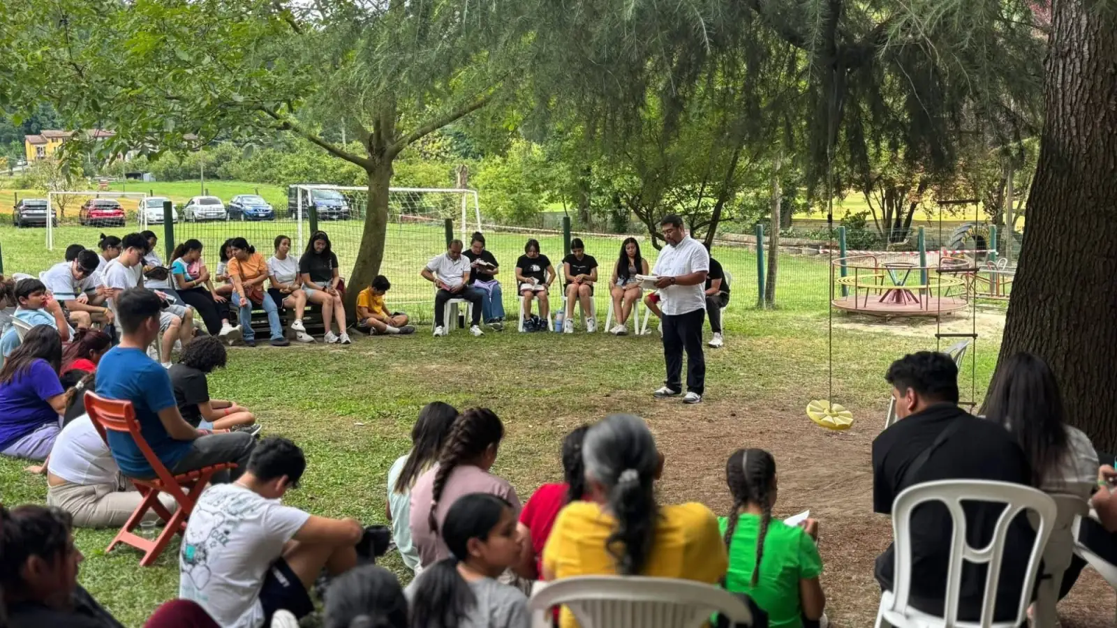 Jóvenes y familias sentados en círculo al aire libre durante un momento de lectura de la Biblia