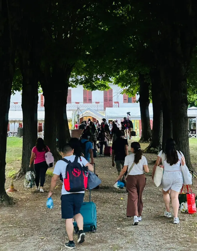 Un grupo de personas con maletas y bolsas camina por un camino con árboles