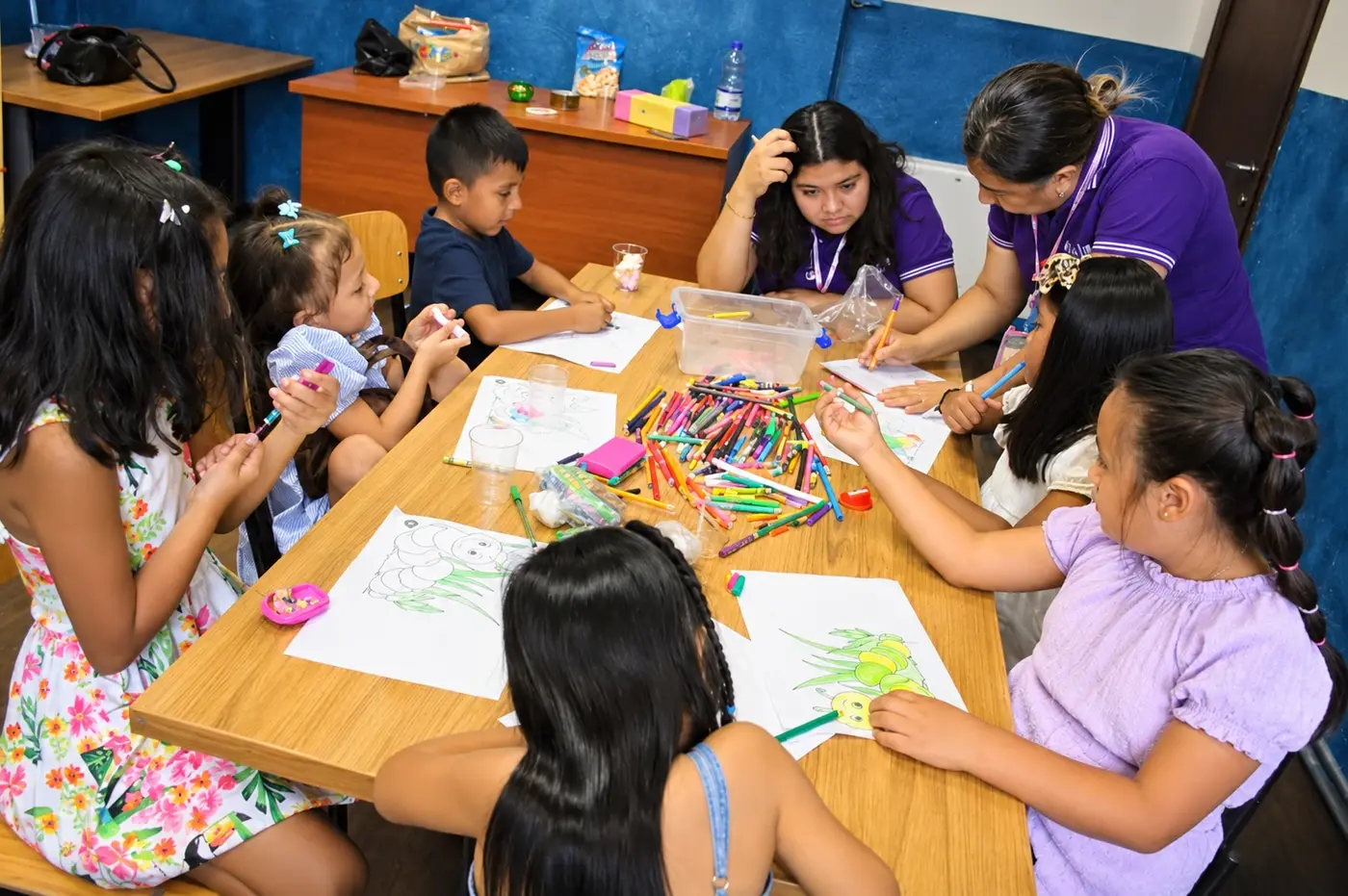 Niños coloreando en la mesa con las maestras durante la Escuela Bíblica